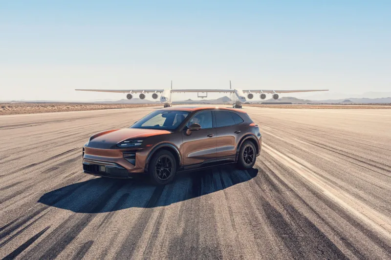 Вид на кроссовер Porsche Cayenne, движущийся под крыльями гигантского авиалайнера Roc